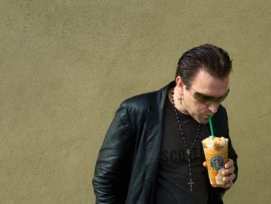 Pavel Sfera as Bono drinking from a Starbucks cup